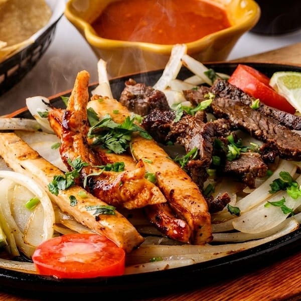Sizzling chicken and beef fajitas with onions, tomatoes, and lime in a cast iron skillet.