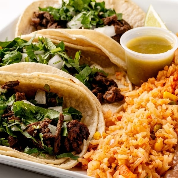 Three carne asada street tacos with cilantro and onions, served with rice and refried beans.